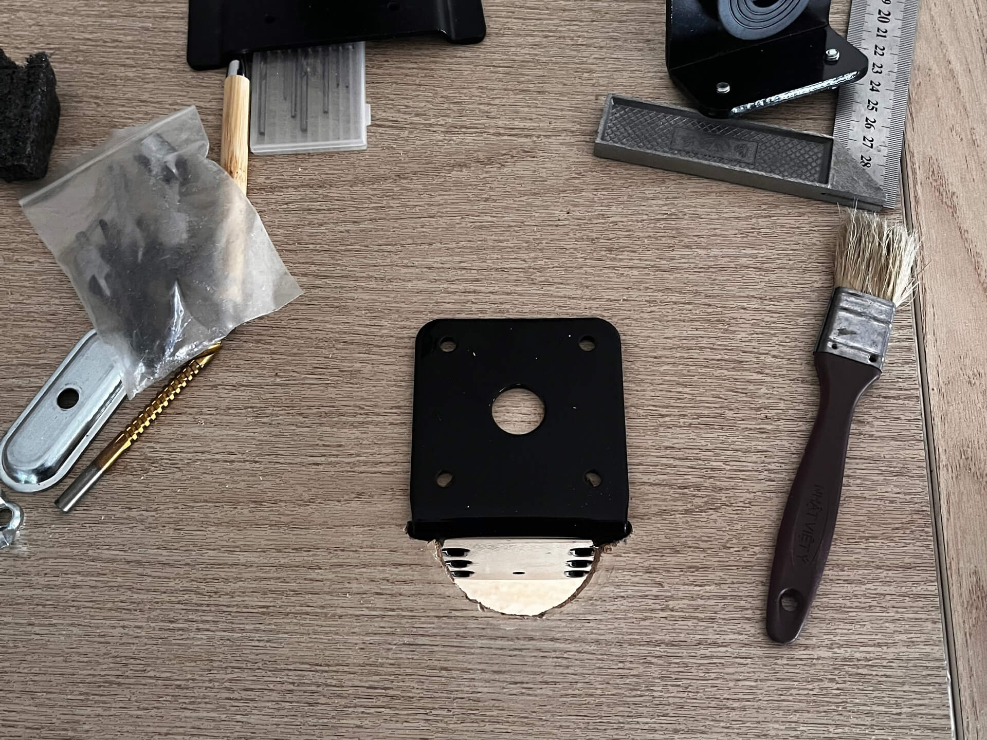 Drill, bits, ruler and cleaning brush arranged on flat wooden tabletop next to black monitor mounting hardware
