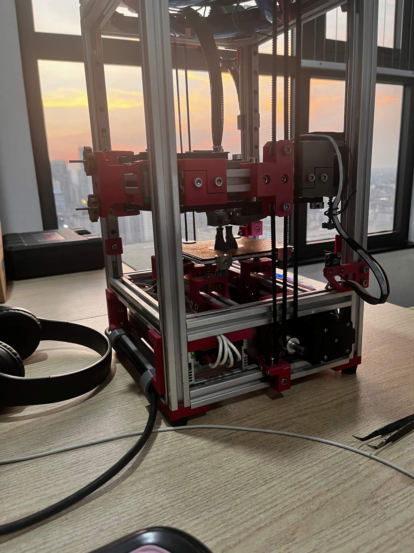 3D printer operating smoothly on flat tabletop with orange sunset and city skyline visible through clear windows