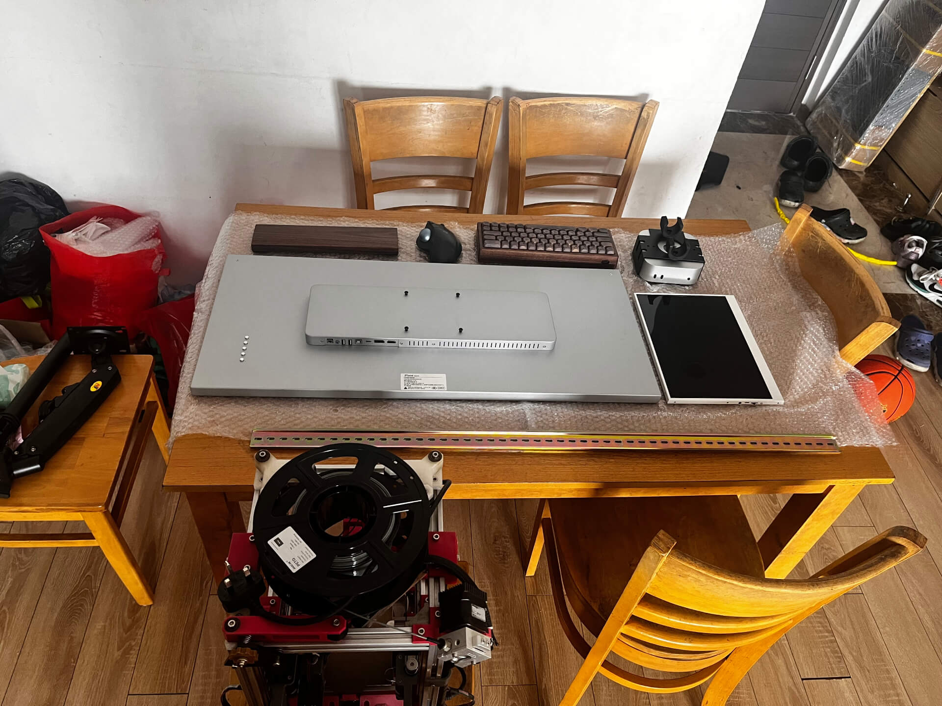 Computer monitor, keyboard, 3D printer components and various workshop tools organized on wooden dining table