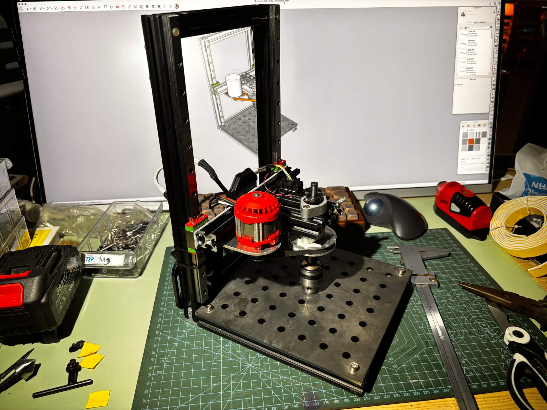 Completed DIY press drill on workbench with SketchUp 3D model visible on monitor in background showing design-to-reality comparison