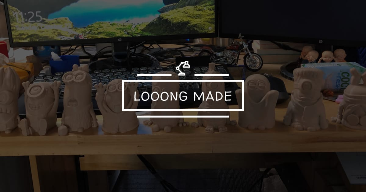 A full row of 3D printed Minion figures displayed on a wooden desk in front of a dual-monitor setup.